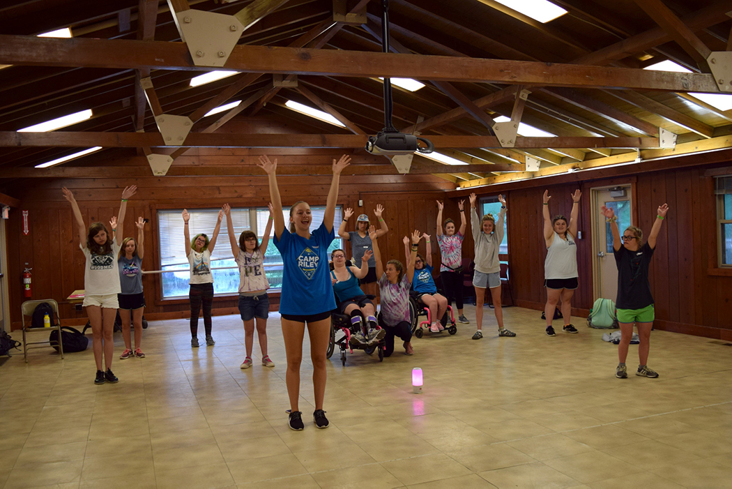 A group of campers follow an instructor by raising their hands.